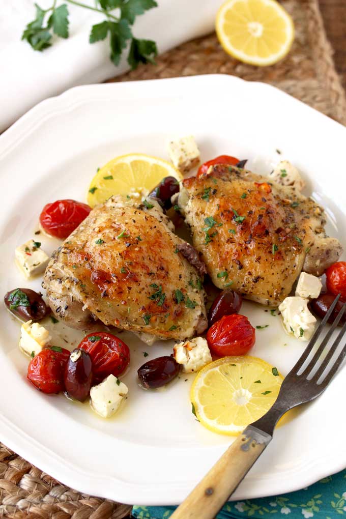 Two pieces of oven roasted chicken thighs on a white plate. 