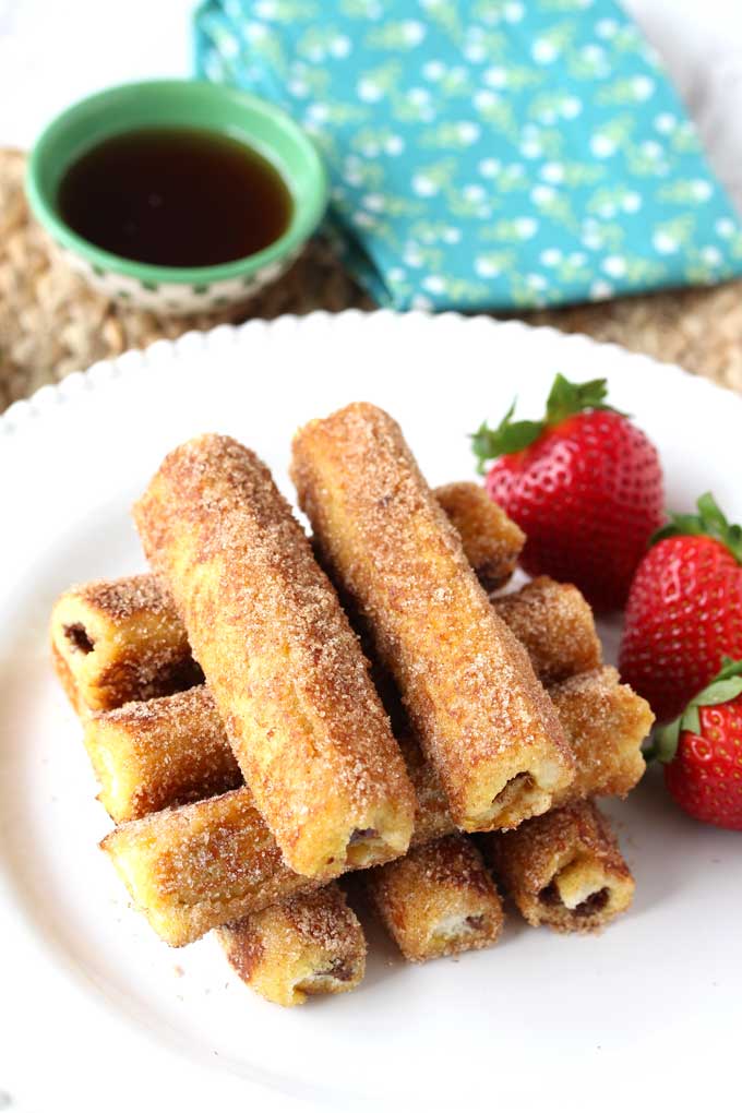 Stack of Nutella French Toast Roll-Ups on a white plate garnished with strawberries