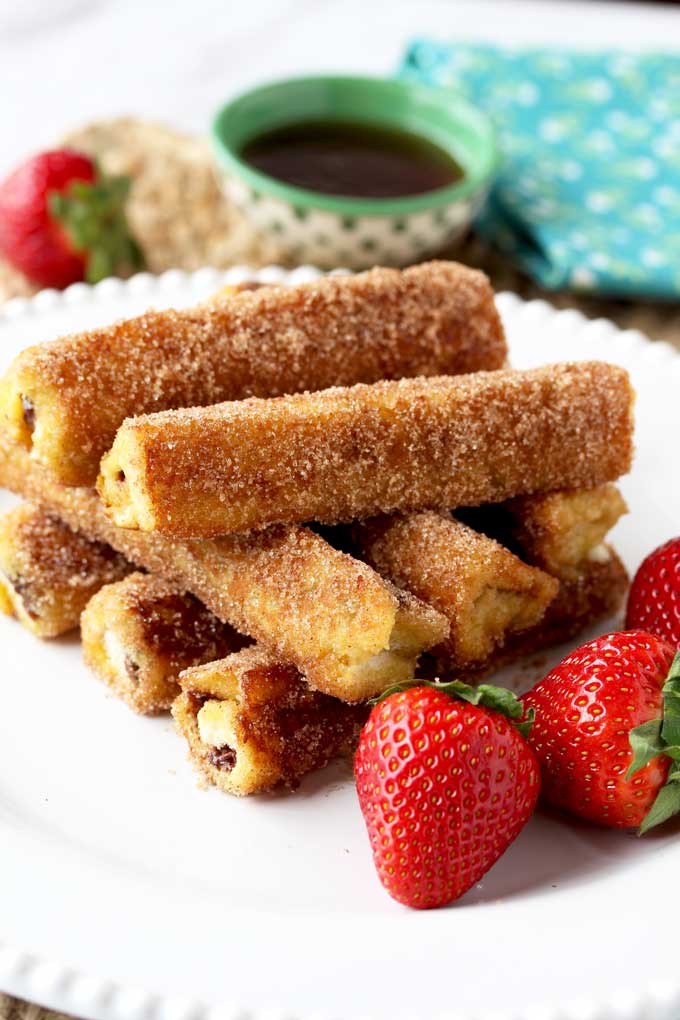 A tall stack of Nutella French Toast Roll-Ups on a white plate with strawberries