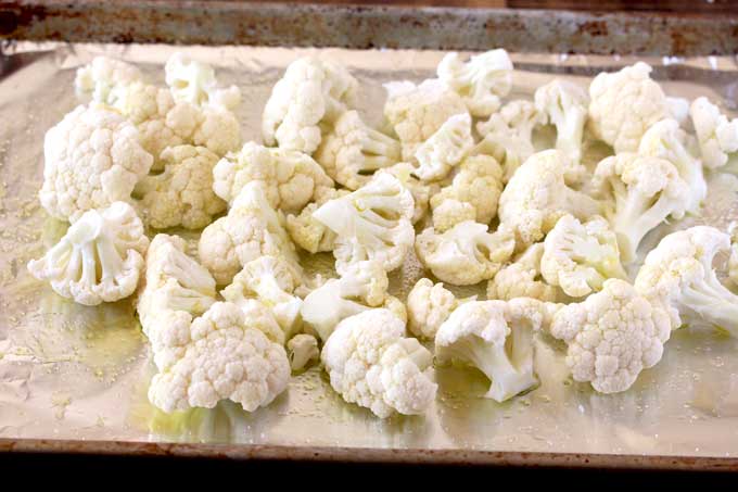 Raw cauliflower florets drizzled with olive oil on a baking sheet pan