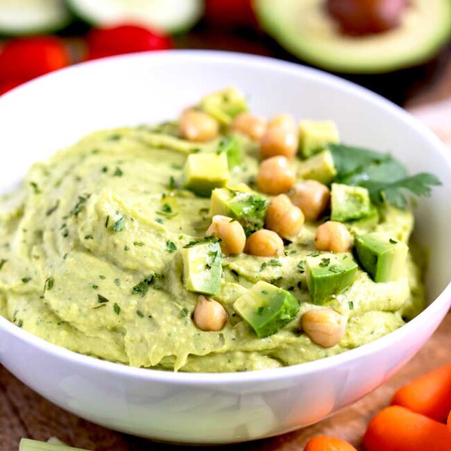 Avocado Hummus in a white serving bowl garnished with avocado and chickpeas.