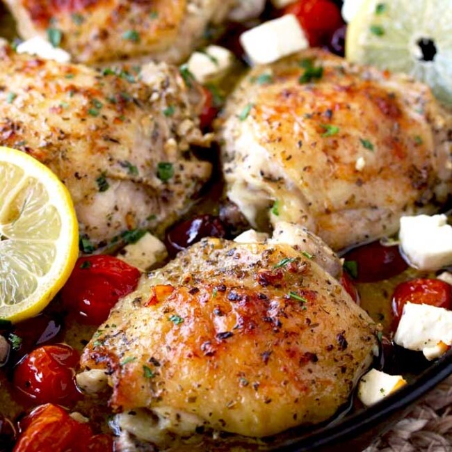 Greek Lemon Oven Roasted Chicken Thighs in a cast iron skillet with roasted tomatoes, Kalamata olives and Feta cheese