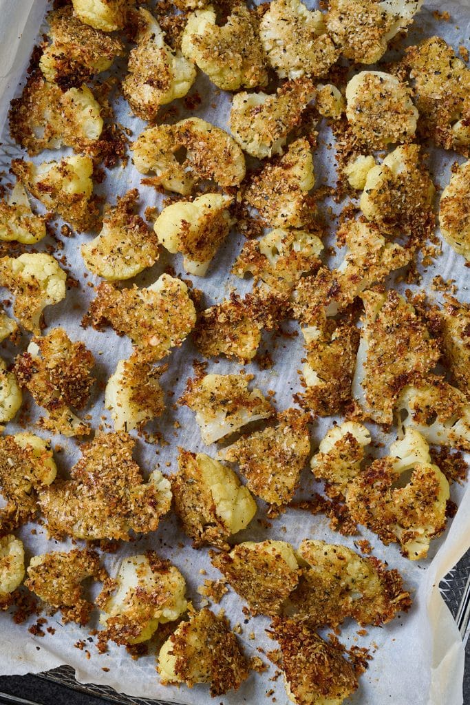Cauliflower florets with an extra crispy coating on a baking pan.