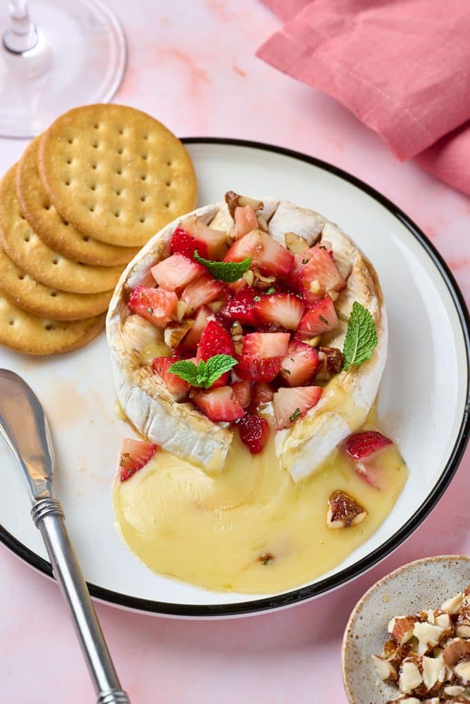 Melty baked brie cheese topped with strawberries on a white plate
