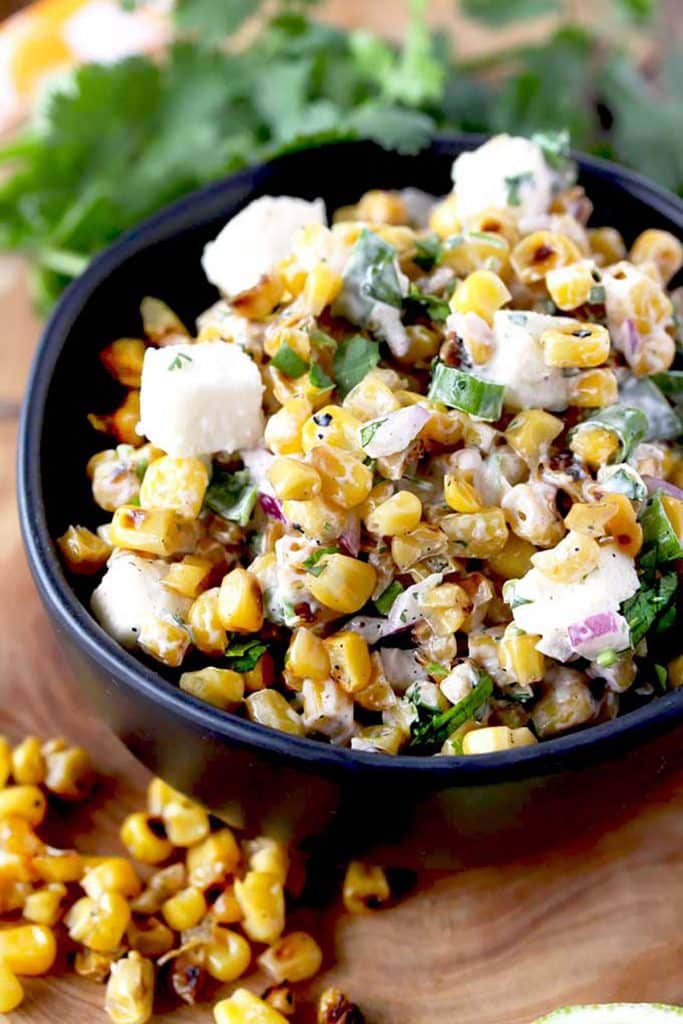 A black salad bowl filled with creamy roasted corn salad