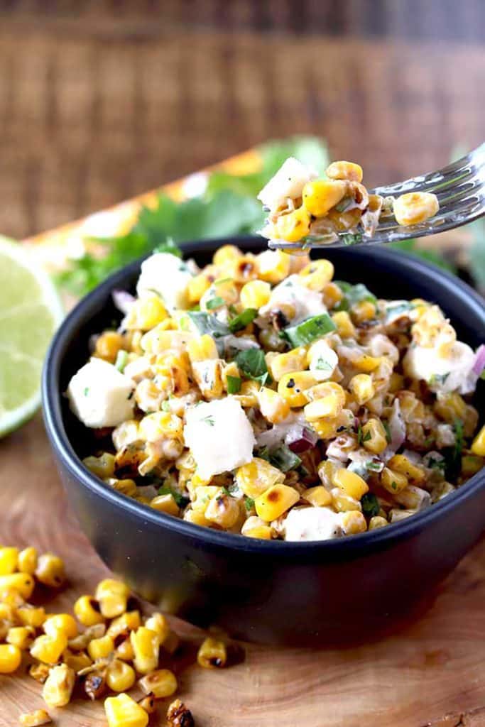 A fork lifting roasted corn salad from a salad bowl