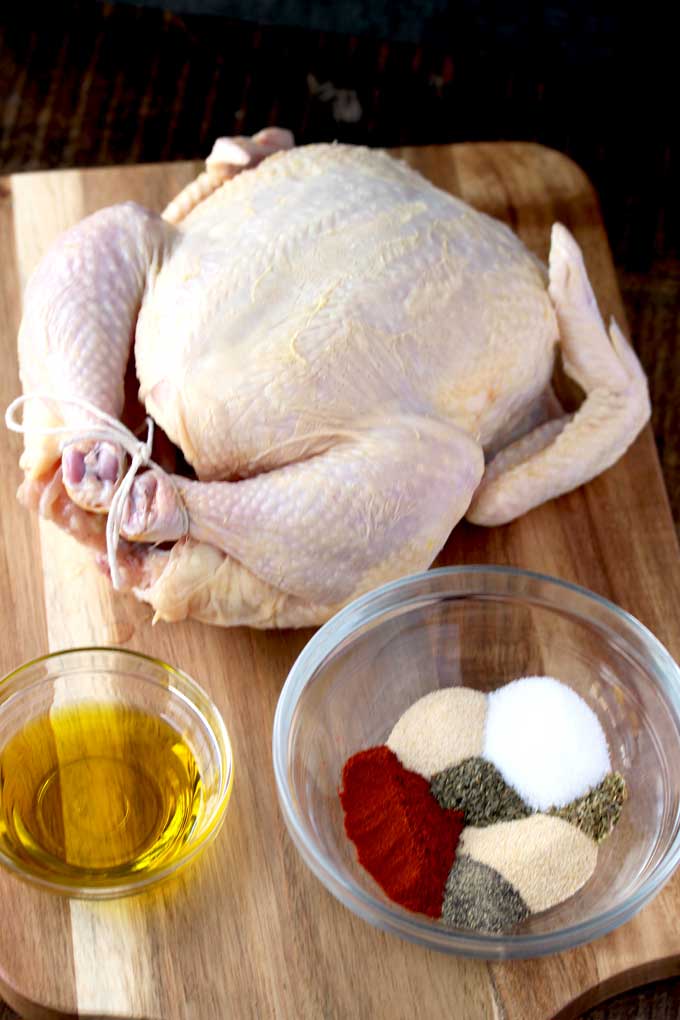 Ingredients to make Instant Pot Rotisserie Chicken, a whole chicken, olive oil and seasoning mix on a wooden board