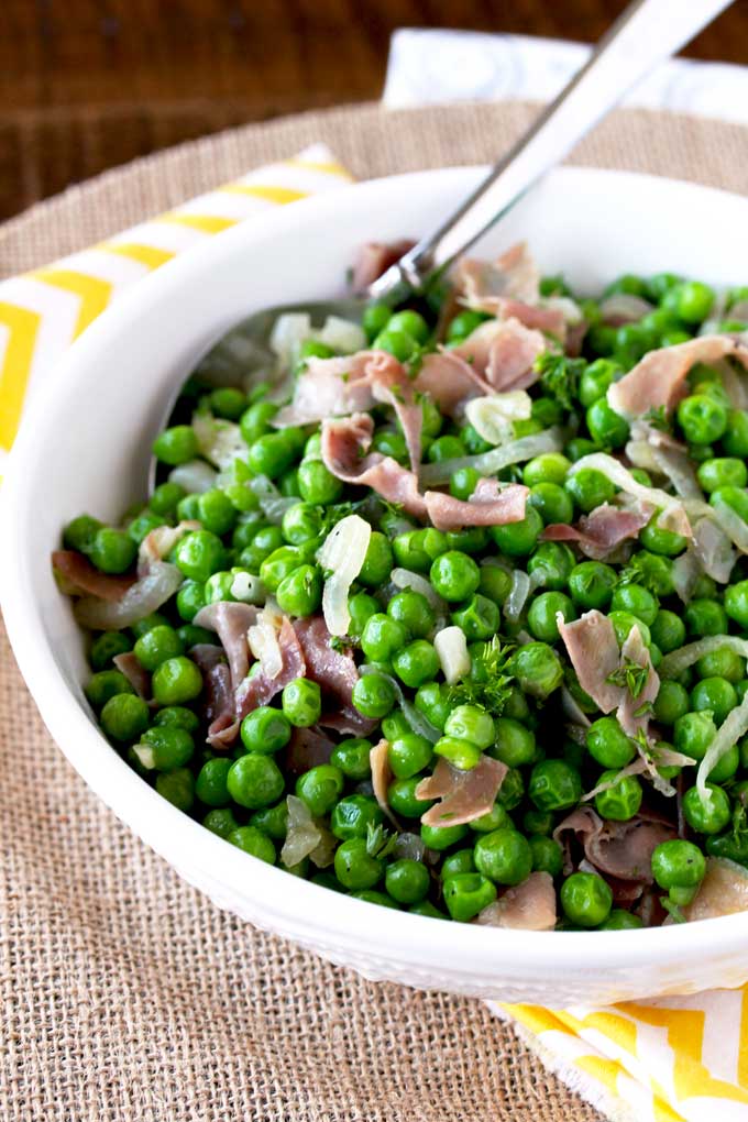 White bowl with sauteed peas with prosciutto and shallots.