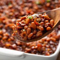 Homemade baked beans served with a wooden spoon from a white baking dish