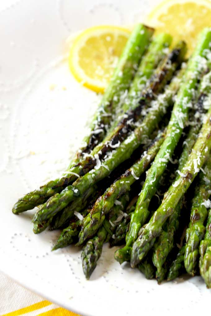 Grilled Asparagus tossed in lemon garlic butter and sprinkled with Parmesan cheese on a white plate