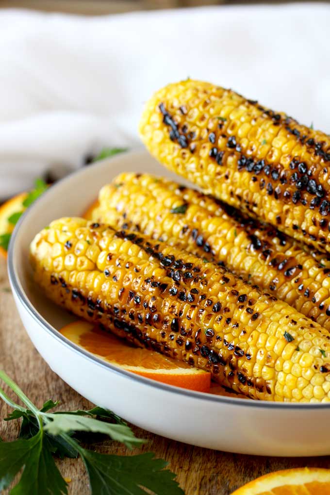 A stack of grilled corn on the cob on a white plate