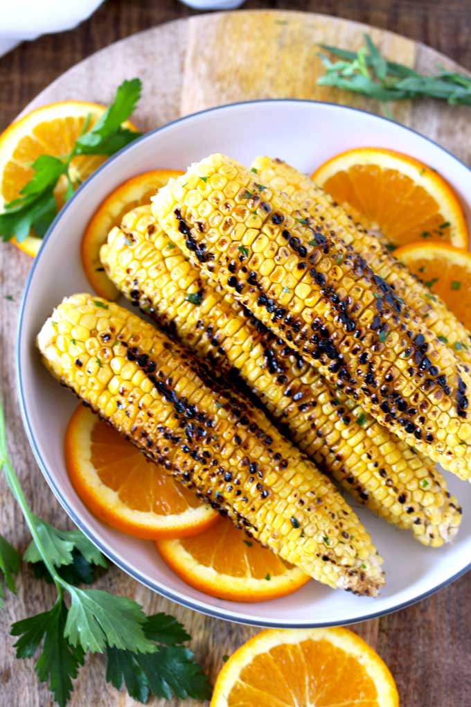 Grilled Corn on a white plate garnished with orange slices
