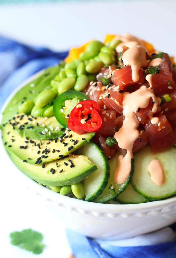 A bowl filled with chunks of fresh tuna, avocado, edamame and topped with a sauce and sesame seeds.