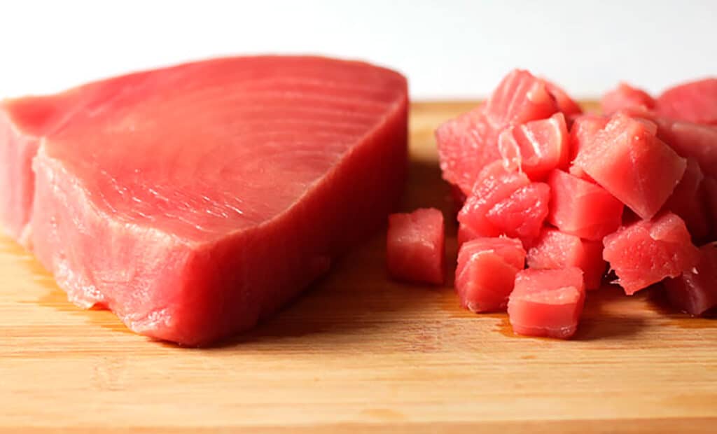 A piece of fresh sushi grade tuna and some diced tuna on a wooden cutting board.