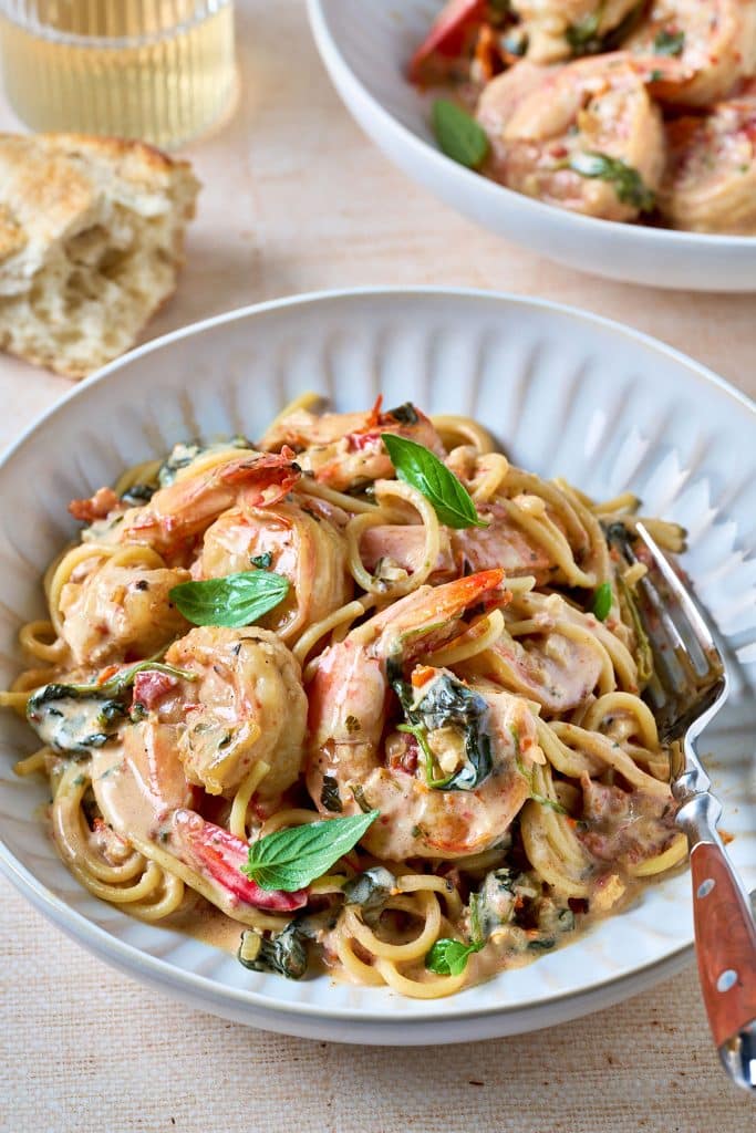 tuscan shrimp tossed with spaghetti in a white serving bowl