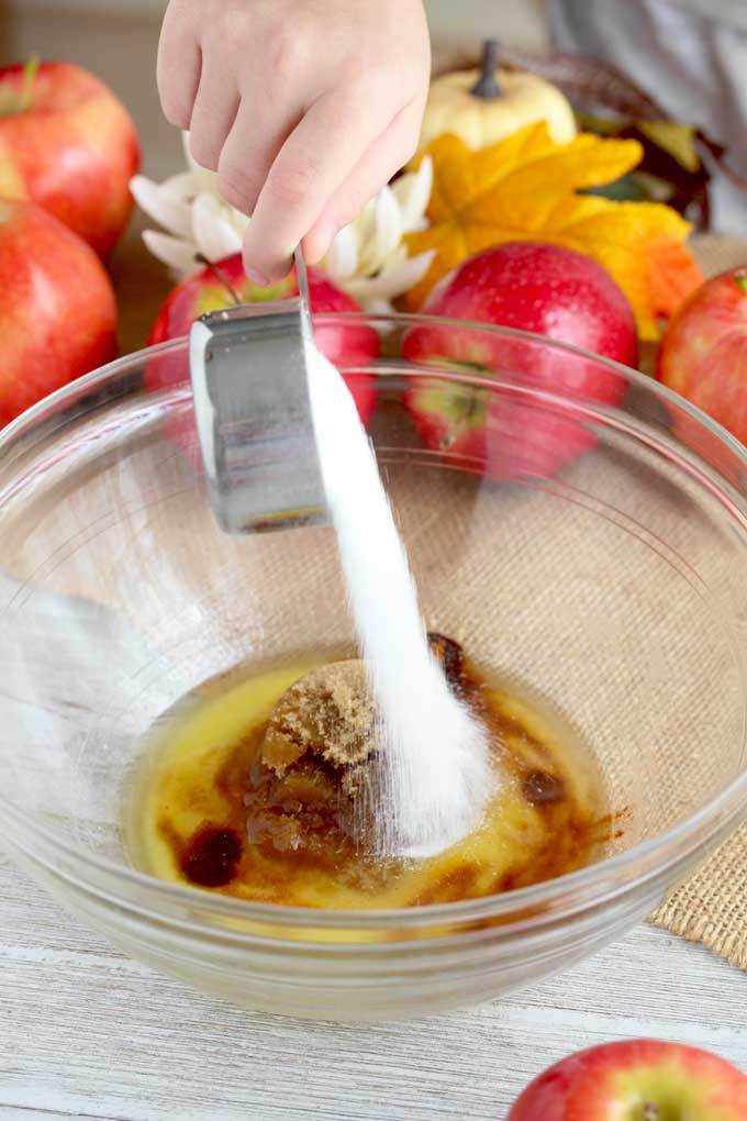 Sugar is been poured in a bowl with melted butter, cinnamon and brown sugar.