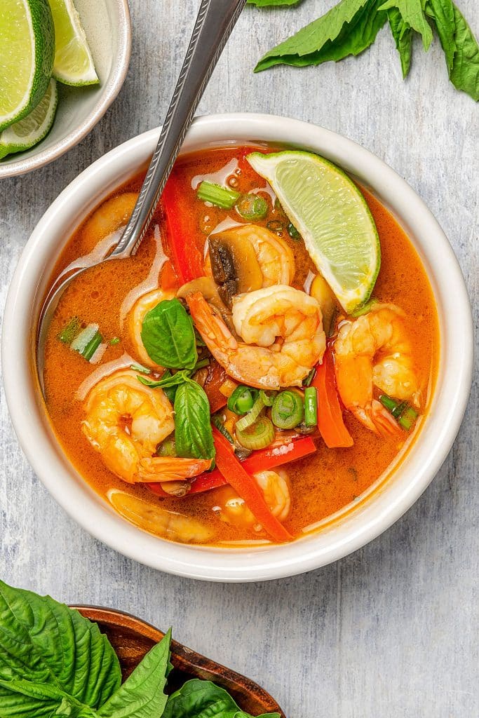 A bowl of Thai coconut curry soup with large succulent shrimp, garnished with lime wedges