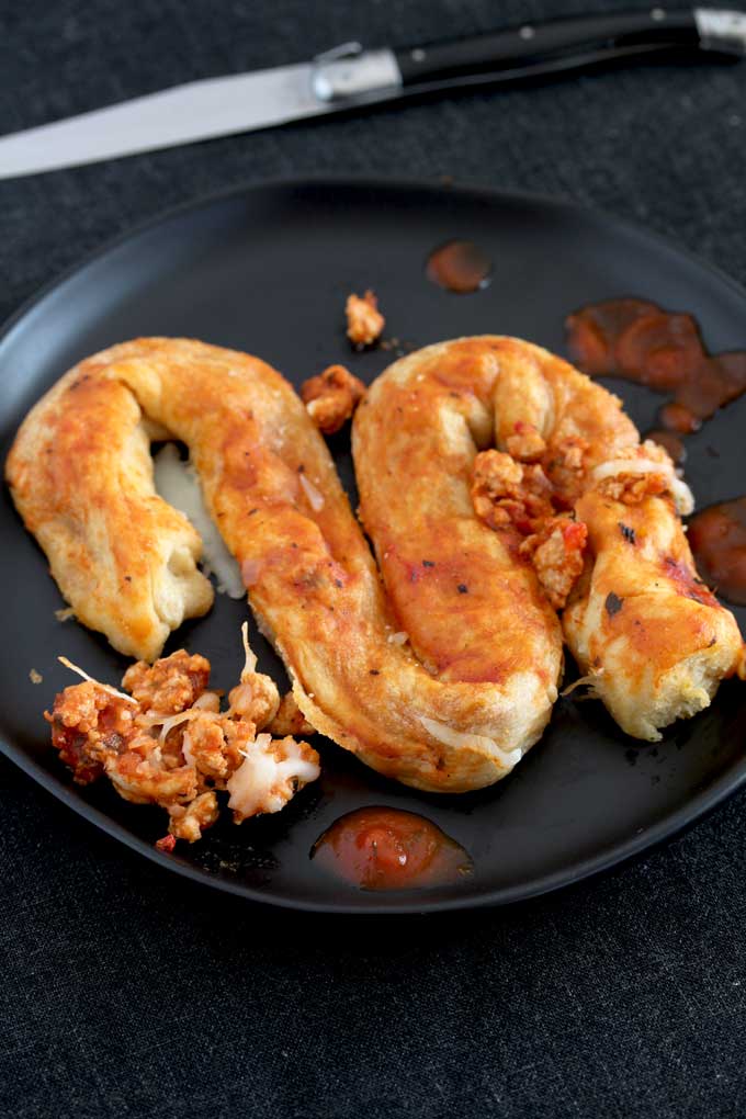 A serving of stuffed crescent roll intestines on a black plate