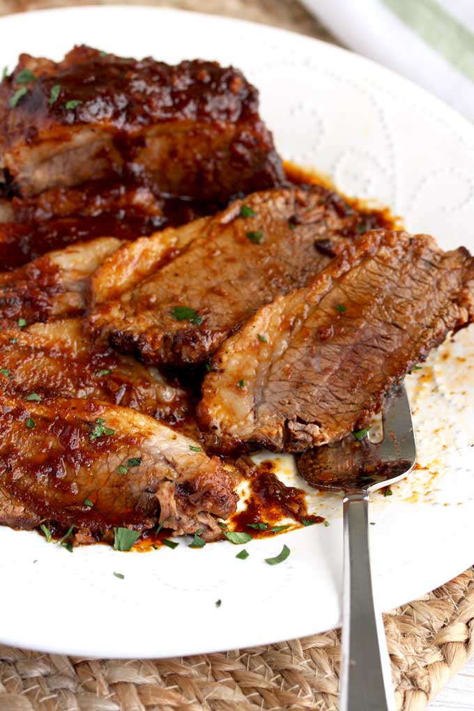 Sliced instant pot beef brisket smothered in BBQ sauce on a white platter.