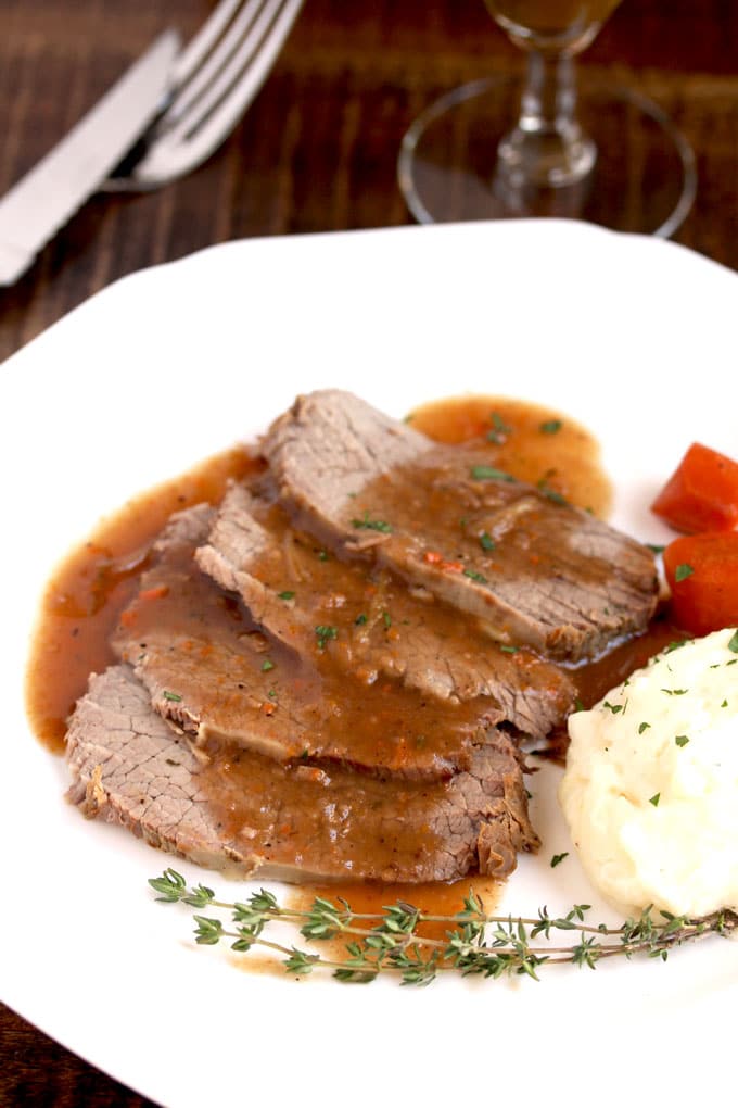 Slices of sauerbraten with mashed potatoes and carrots on a white plate.