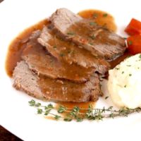 Slices of saurbraten with mashed potatoes and carrots on a white plate.