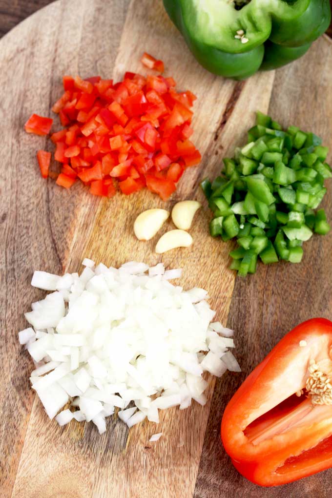 Chopped onions, red and green bell peppers and garlic on a cutting board