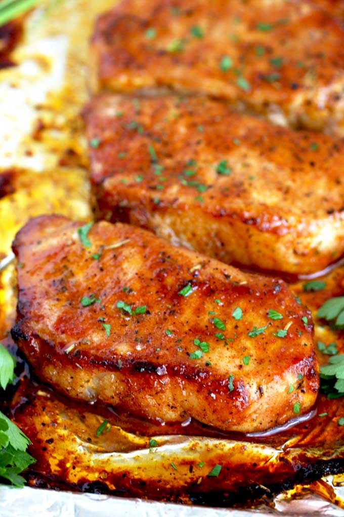 Several golden and juicy pork chops on a sheet pan coming out from the oven.