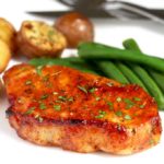 Oven Baked Pork Chops with roasted potatoes and green beanson a white plate