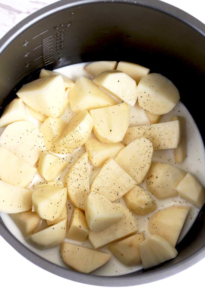 Raw chopped potatoes with broth and milk inside the pressure cooker.