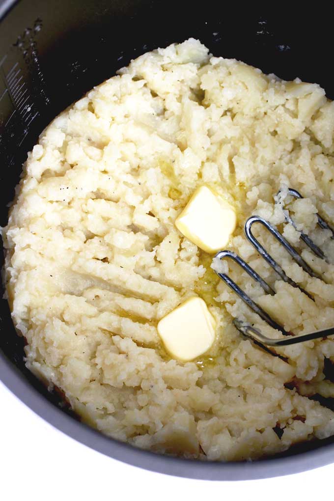 Potatoes, butter and a masher inside a pressure cooker.