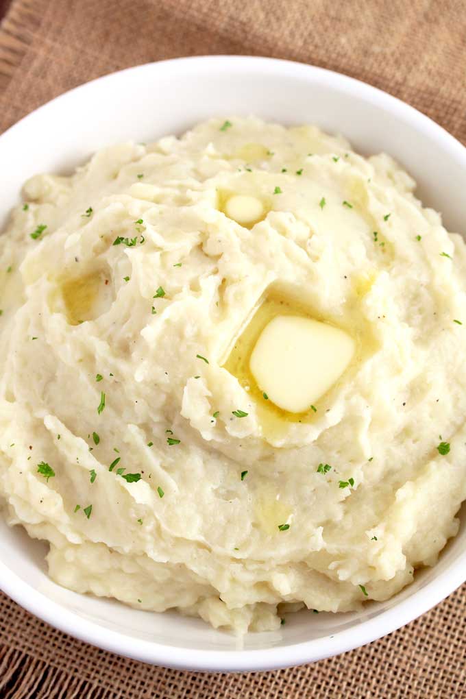 Creamy slow cooker mashed potatoes topped with a bit of butter served on a white bowl.
