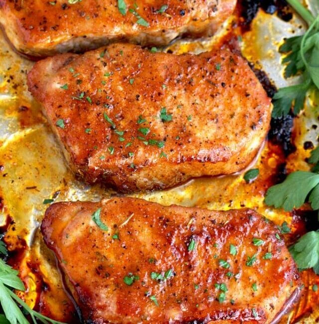 Several golden and juicy pork chops on a sheet pan coming out from the oven.