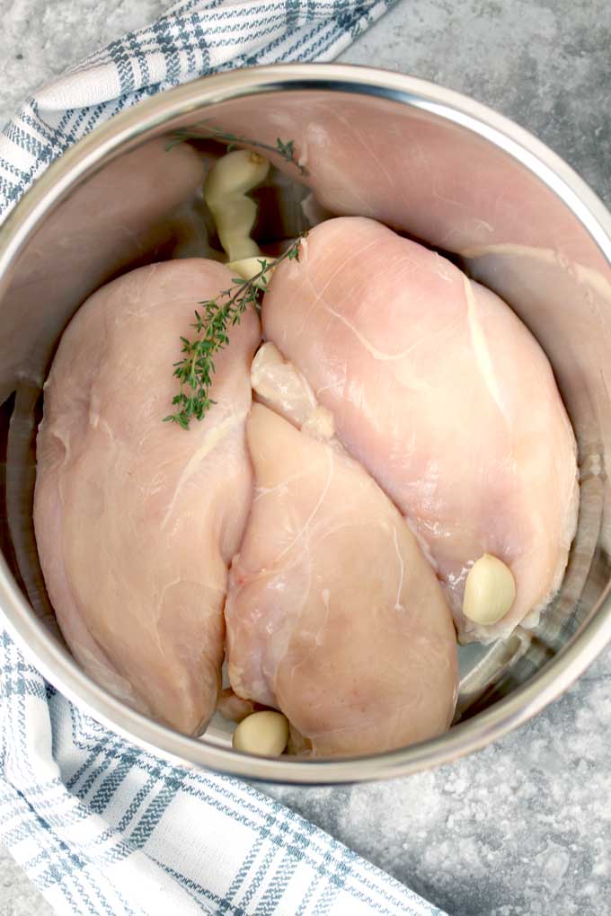 Raw chicken breasts in the instant pot with garlic cloves and fresh thyme.