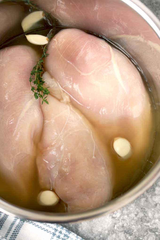 Raw chicken breasts in the instant pot with garlic cloves, fresh thyme. and broth.