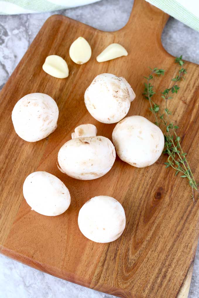 Mushrooms, garlic cloves and fresh thyme on a cutting board.