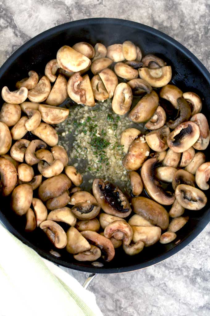 Mushrooms cooking with chopped garlic and thyme in a skillet.