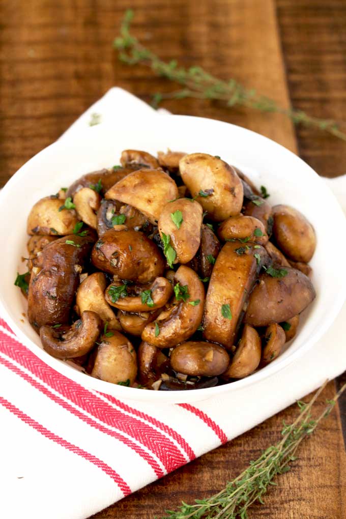 Sauteed mushrooms with garlic butter and herbs served on a white bowl.