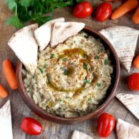 Baba Ganoush in a wooden serving bowl served with pita bread, baby carrots and tomatoes.