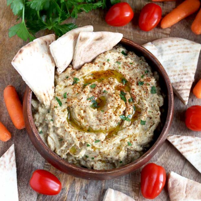 Baba Ganoush in a wooden serving bowl served with pita bread, baby carrots and tomatoes.