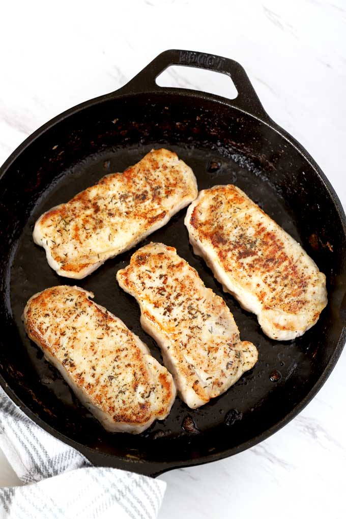 Golden pan seared pork chops in a skillet.