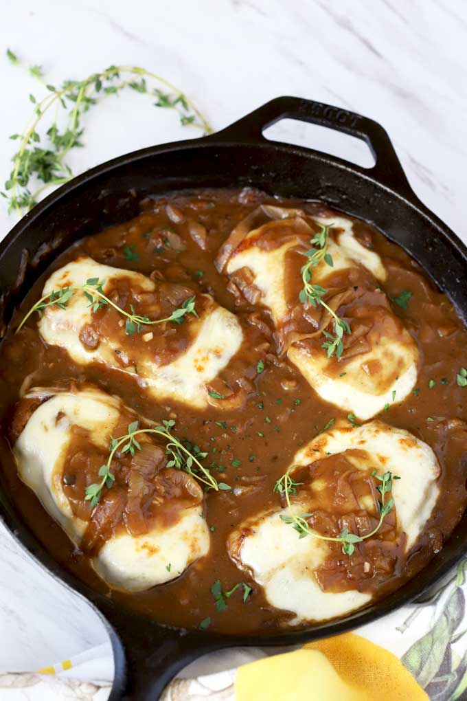 Smothered Pork Chops topped with gooey cheese in a skillet.