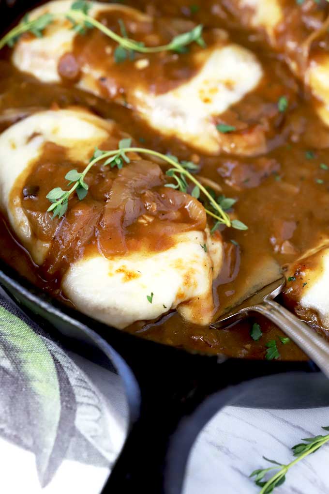 Smothered pork chops lift by a serving spoon from a cast iron skillet.