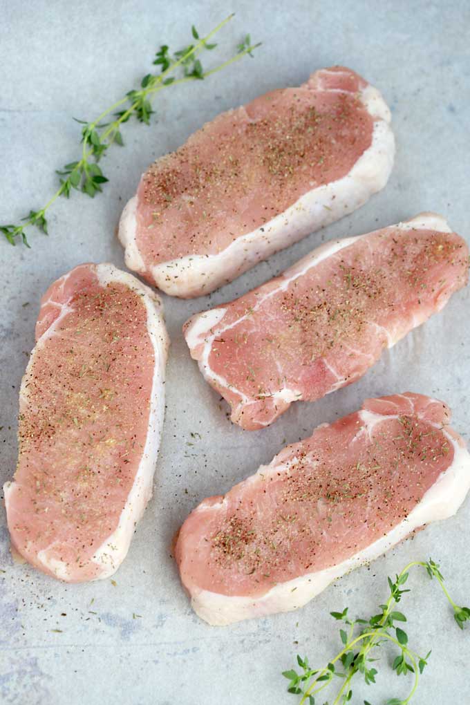 Seasoned raw pork chops on a white surface.