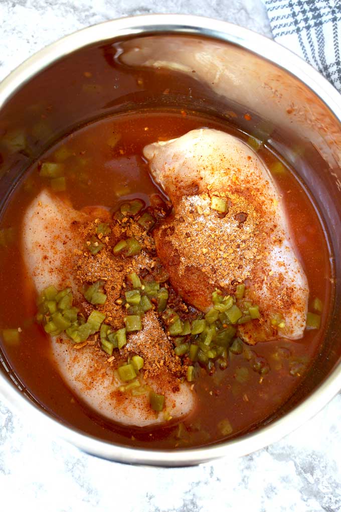 Chicken breast topped with the ingredients to make this dish inside a pressure cooker.