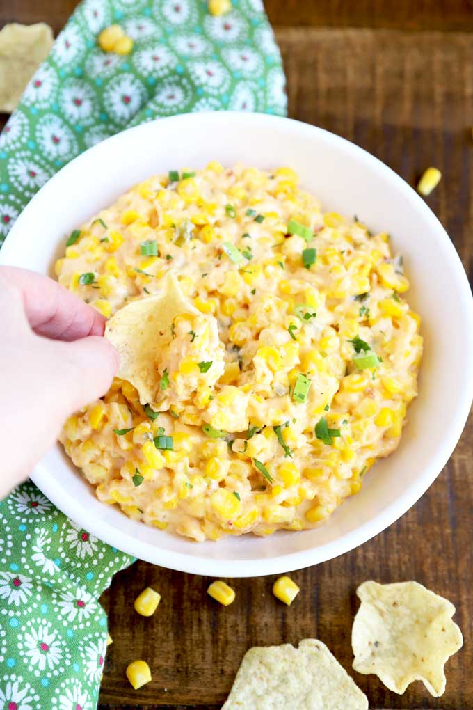 Tortilla chip scooping corn dip from a white bowl.