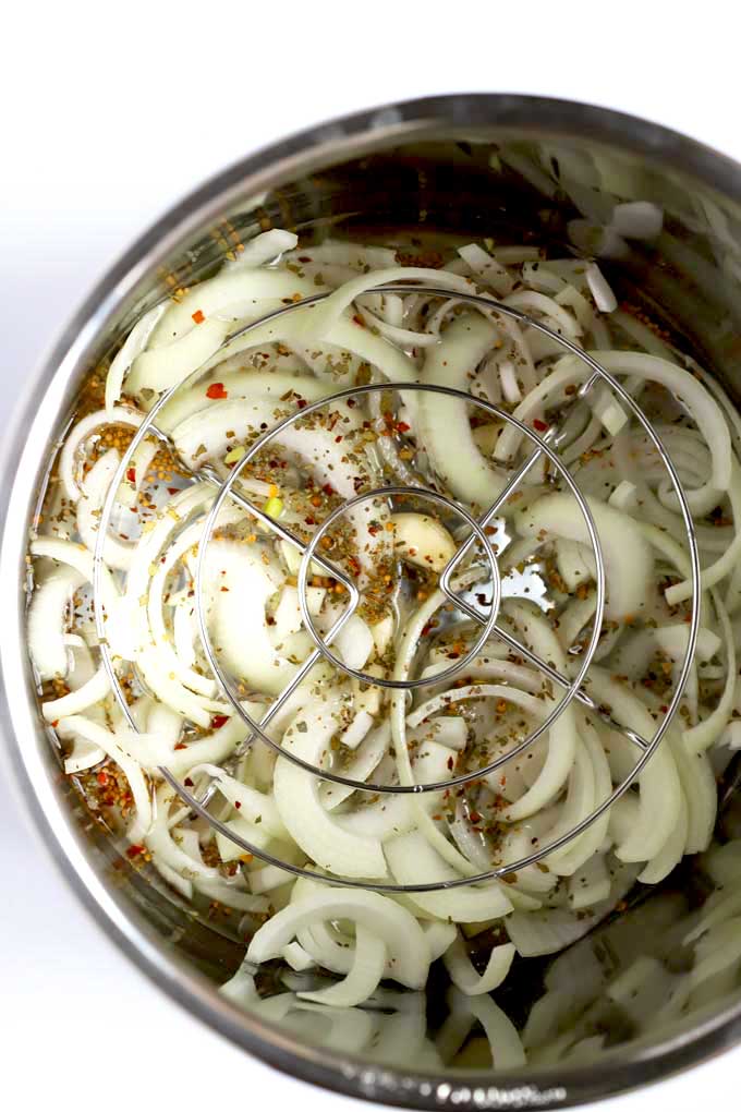 Sliced onions, garlic, pickling spices, broth and beer inside the instant pot.