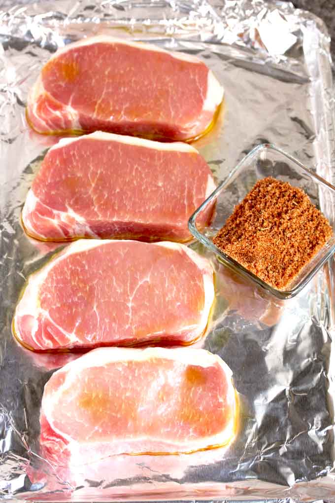 Raw pork chops on a sheet pan and a bowl of dry rub mix.