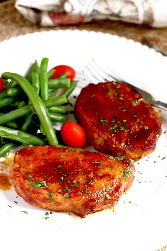 Two Baked Pork Chops on a white plate.