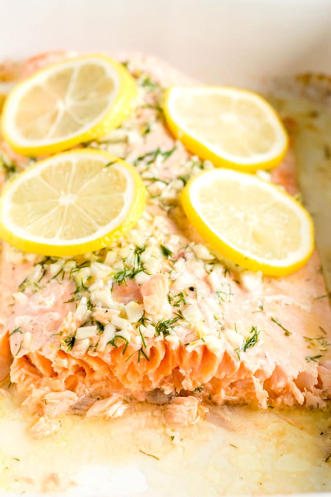 A piece of salmon filet baked and topped with lemon inside a baking dish.