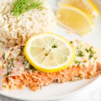 A piece of salmon served with rice and garnished with sliced lemons.